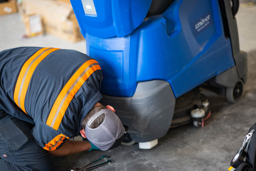 A WaySolutions technician uses hand tools to repair the lower scrub deck of a blue Kärcher Chariot iScrub 20X floor scrubber in Layton, Utah.

